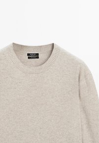 Ljust beige cashmeretröja med rund hals och ribbat detaljarbete på kragen och axlarna, med en slät textur och minimalistisk design.