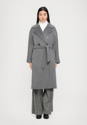 Cappotto lungo in misto lana grigio con colletto a laccio, cintura annodata, chiusura a doppio bottone e tasche laterali, abbinato a pantaloni grigi a gamba larga.