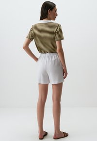 Camicia a maniche corte a righe gialla, marrone e bianca; pantaloni corti bianchi con vita elasticizzata; sandali casual; sfondo neutro.