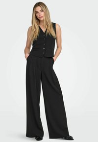 Zwart op maat gemaakt vest met een V-hals en knopen, gecombineerd met hoogwaardige wijde pijpenbroek met hoge taille. Gladde textuur en minimalistisch ontwerp.