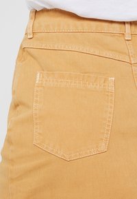 Pantalones de mezclilla amarillos claros que presentan un bolsillo trasero de forma rectangular, costuras en contraste y un acabado de textura suave.