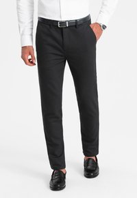 Pantalons noirs ajustés avec une texture lisse, coupe droite et poches pratiques. Associés à des mocassins noirs et une chemise blanche à boutons.