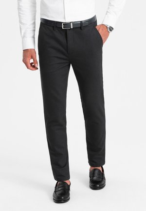 Pantalones negros a medida con una textura suave, corte recto y bolsillos prácticos. Combinados con mocasines negros y una camisa blanca de botones.