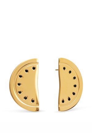 Pendientes dorados en forma de semicírculo con detalles negros en forma de lágrima dispuestos como semillas de sandía sobre un fondo blanco.