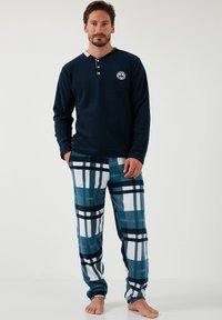 Marineblaue Langarmbluse mit zwei Knöpfen und einem Logo, kombiniert mit teal- und weißen karierten Fleecehosen. Weicher Stoff, lässige Passform.