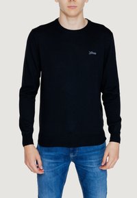 Maglione nero a girocollo realizzato in tessuto morbido, con polsini e orlo a costine, dotato di un piccolo logo ricamato sul petto. Abbinato a jeans blu.