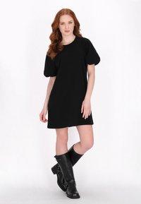 Rochie scurtă neagră cu mâneci bufante, realizată dintr-un material moale. Purtați cu cizme din piele neagră până la genunchi, cu detalii metalice.