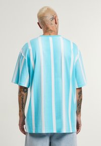 Turkio ir baltos juostelės oversized marškiniai, pagaminti iš švelnaus medvilnės audinio, su trumpomis rankovėmis ir apvaliu iškirpimu.