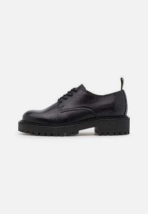 Black leather lace-up shoe with chunky lug sole and heel tab, side view on plain light gray background.