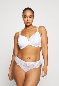 Soutien-gorge blanc en tissu lisse avec des bonnets structurés, associé à des culottes en dentelle blanche avec des bords festonnés et des motifs floraux.