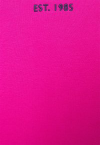 Magenta bomuldsstof med en glat tekstur, der har sort broderet tekst "EST. 1985" i det øverste område, centreret horisontalt.