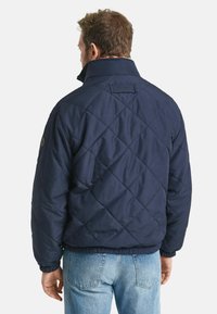Marineblauwe gevoerde jas met een staande kraag, elastische manchetten en een logotab aan de achterkant. Het ontwerp heeft een ruitvormig stiksel.