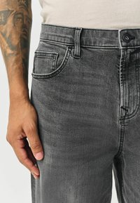 Mørkegrå denimjeans med klassisk fem-lomme-design, kontrastsyninger og knaplukning i taljen. Glat tekstur.