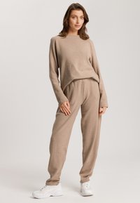 Helles braunes Lounge-Set bestehend aus einem langärmligen Oberteil mit lockerem Schnitt und passender, taillierter Hose, aus weichem, strukturiertem Stoff gefertigt.