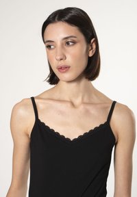 Camisola nera realizzata in morbido tessuto, con delicata rifinitura in pizzo scallop lungo il collo e spalline regolabili.