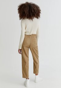 Pull en maille côtelée crème et pantalon en velours côtelé beige taille haute avec poches avant et arrière. Des baskets blanches complètent la tenue.