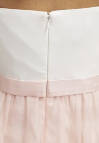 Robe blanche avec un corsage ajusté et une jupe en tulle rose. Possède une fermeture éclair au dos et une ceinture en satin. La texture lisse du tissu contraste avec la transparence de la jupe.