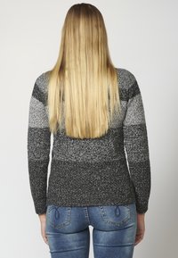 Grijs en zwart gebreid sweater met lange mouwen, met een gestructureerd ontwerp en kleurverloop. Gecombineerd met blauwe denim jeans.