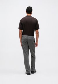 Rjava kratka polo majica oblečena z sivo volnenimi hlačami. Hlače imajo stranske žepe in gladko teksturo, dopolnjene z črnimi čevlji.