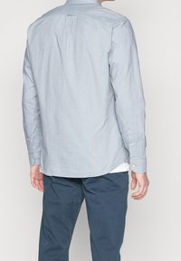 Ljust blå knappad skjorta i bomull med mjuk textur, med en ryggveck, långa ärmar och rundad fåll.