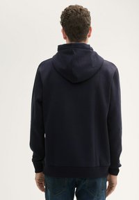 Felpa con cappuccio blu navy con finitura testurizzata, polsi e vita elasticizzati. Presenta una tasca a marsupio e un design dal taglio morbido.