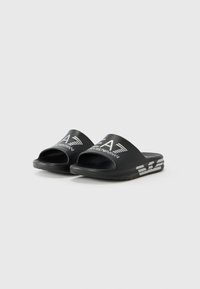 Black slide sandals with an open toe design, featuring a matte finish and white logo accents on the upper and side. Textured outsole.