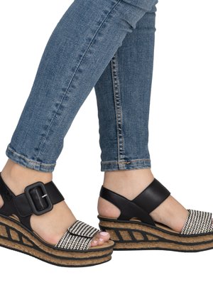 Feet wearing black and white wedge sandals with cork soles, paired with blue denim jeans.
