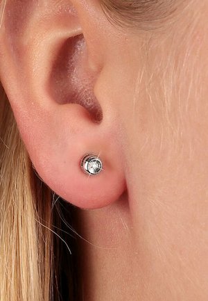 Silberne Steckerohrringe mit einem runden, klaren Stein. Glatte Metalloberfläche, klein in der Größe, liegt eng am Ohrläppchen an.