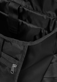 Svart tygväska med en slät interiör, som har flera fack, en dragkedjeficka och förstärkta sömmar.