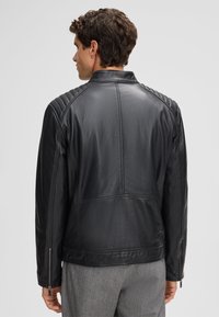 Giacca di pelle nera con dettagli trapuntati sulle spalle, colletto alto e tasche con zip, progettata con una texture liscia e una vestibilità sartoriale.
