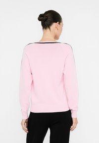 Helles rosa Sweatshirt mit langen Ärmeln, runder Halslinie und schwarzemBesatz an den Schultern. Stricktextur mit gerippten Bündchen und Saum.