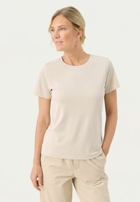 T-shirt beige chiaro a maniche corte con scollatura rotonda, realizzata in tessuto morbido. Indossato con pantaloni beige abbinati, di taglio comodo.