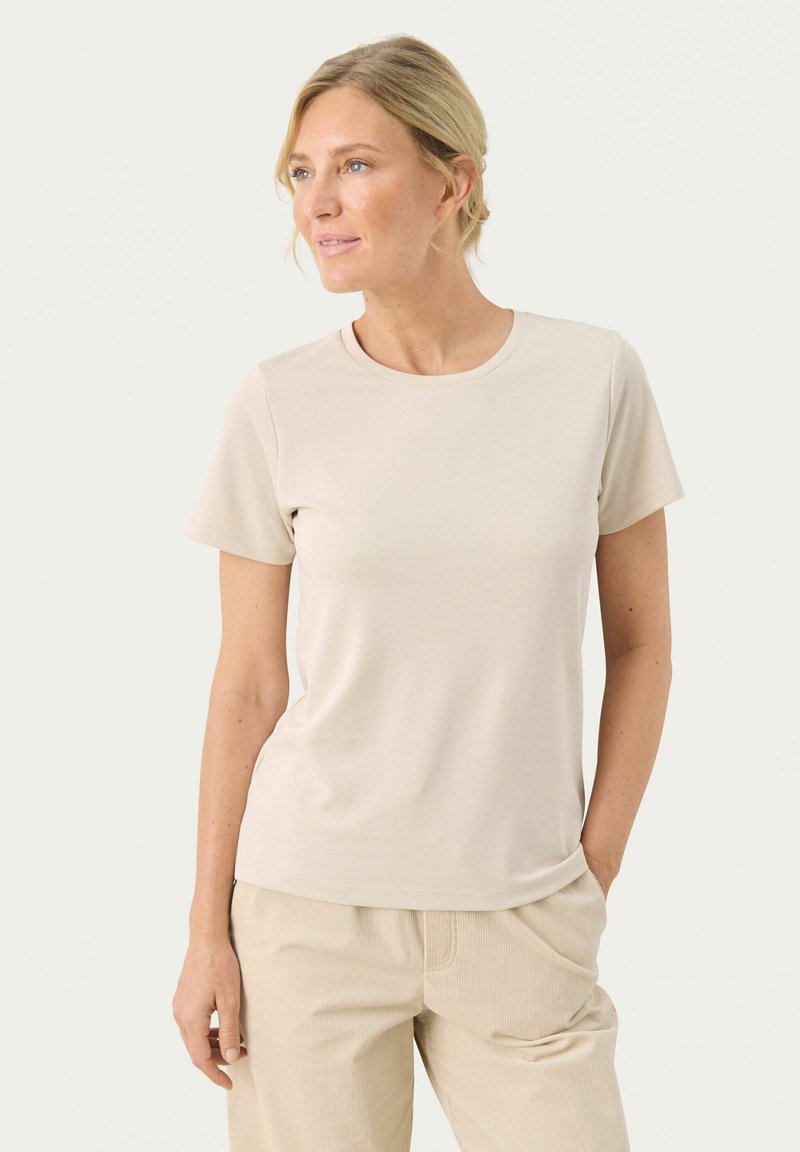 T-shirt beige chiaro a maniche corte con scollatura rotonda, realizzata in tessuto morbido. Indossato con pantaloni beige abbinati, di taglio comodo.
