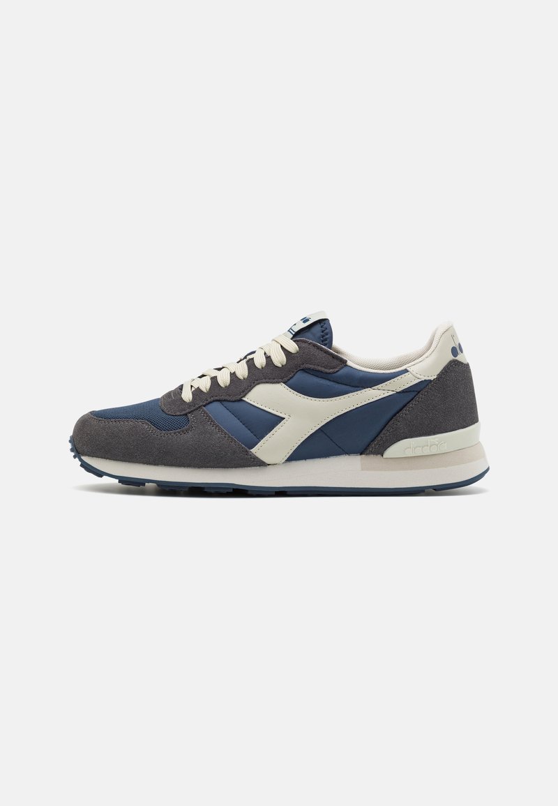 Marineblaue und graue Sportschuhe aus Wildleder und Mesh-Materialien, mit Cremeakzenten, Schnürdesign und einer strukturierten Sohle. Klassische Retro-Silhouette.