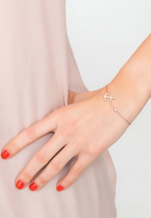 Rose gold bracelet featuring an arrow design embellished with clear crystals and a small round accent. Hand resting gently on a fabric surface.