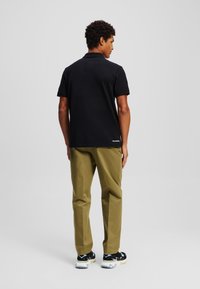 Melna kokvilnas polo krekls ar īsām piedurknēm un ribotu apkakli, apvienots ar olīvzaļām biksēm un melniem sporta apaviem ar ziliem akcentiem.