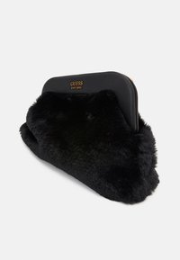 Borsa a mano in pelliccia nera con una parte superiore liscia e strutturata in ecopelle. Presenta un logo dorato "GUESS EST 1981" e una texture morbida.