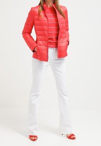 Röd vadderad puffjacka med hög krage, bärs över en röd och vit randig topp, i kombination med vita utsvängda byxor och röda sandaler.