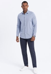 Chemise boutonnée à rayures bleu clair, à manches longues, associée à un pantalon noir marine et des baskets blanches. Tissu lisse, coupe décontractée.