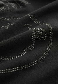 Black fabric features raised rhinestone embellishments forming swirling patterns, highlighting texture and subtle shine against the smooth material.