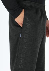 Zwarte heather joggings met een elastische tailleband, voorzien van een zijzak en een klein blauw en geel Zweeds vlagdetail. De tekst "SWEDEMOUNT" is prominent aanwezig.