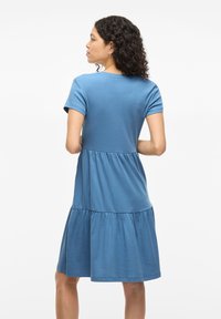 Robe bleue, longueur genoux, en tissu doux, avec des manches courtes et un design de taille à volants. Texture lisse avec des détails de couture subtils.