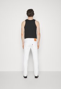 Vita denimjeans med bakfickor, kombinerat med en svart linne. Märkbara egenskaper inkluderar ett sydd logotypmärke på midjebandet.