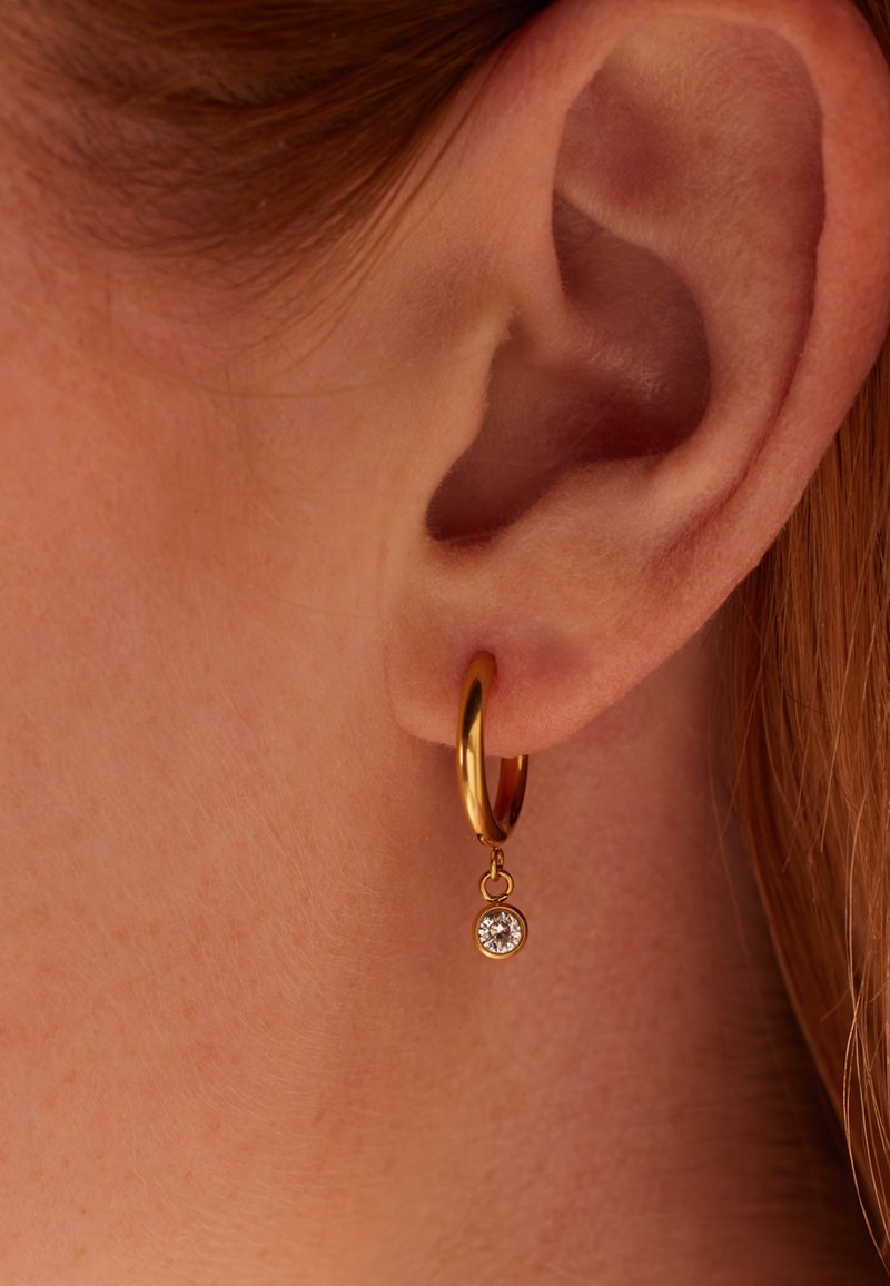Gouden creolen met een hangende heldere rhinestone accent, met een glad oppervlak en cirkelontwerp.