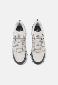Baskets de sport grises et blanches avec un dessus en mesh, des accents rouges contrastants, un bout arrondi et une semelle grise texturée avec des boutons noirs.