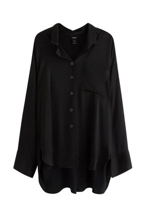Sort langærmet skjorte med knapper, krave, brystlomme og løs pasform, præsenteret på en hvid baggrund.