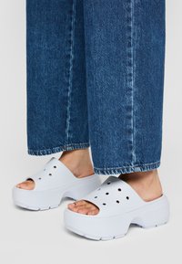 Zoccoli bianchi, durevoli, con fori di ventilazione, design con punta aperta e suola testurizzata. Indossati con pantaloni a gamba larga in denim blu.