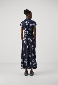 Abito maxi floreale blu navy con maniche corte, presenta motivi floreali azzurri, una vita con lacci e una texture di tessuto morbida.