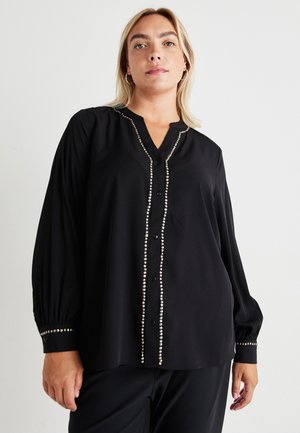 Blusa nera con maniche lunghe, chiusura a bottoni sul davanti e decorativi rivetti argentati lungo la patta e i polsini. Tessuto morbido e liscio.