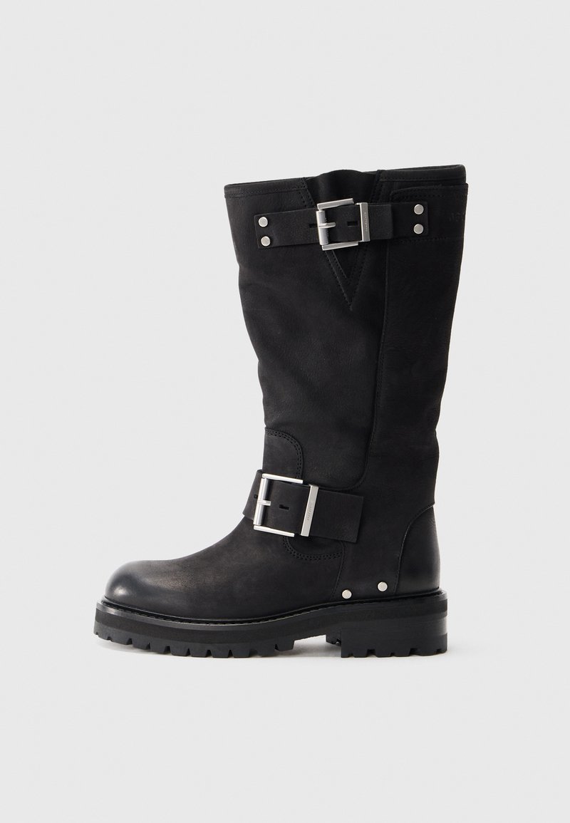 Mustad meesäärde nahast saapad, millel on kaks hõbedast pandlat ja paks jäme tald, esitatud vasakult küljelt valge tausta ees.